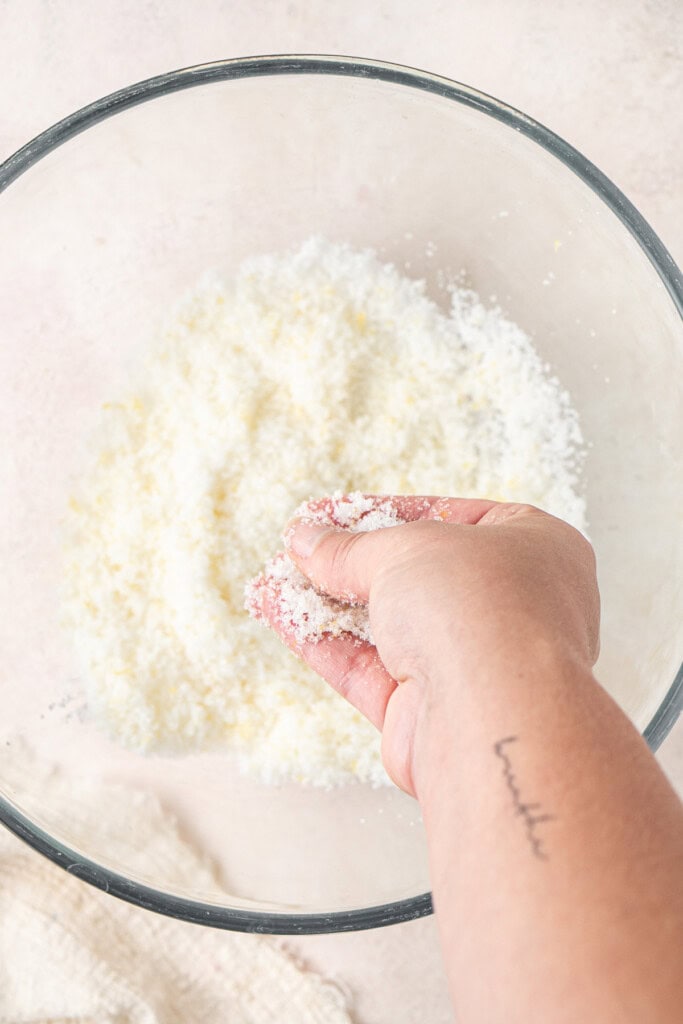 A hand rubbing the lemon zest with the white sugar.