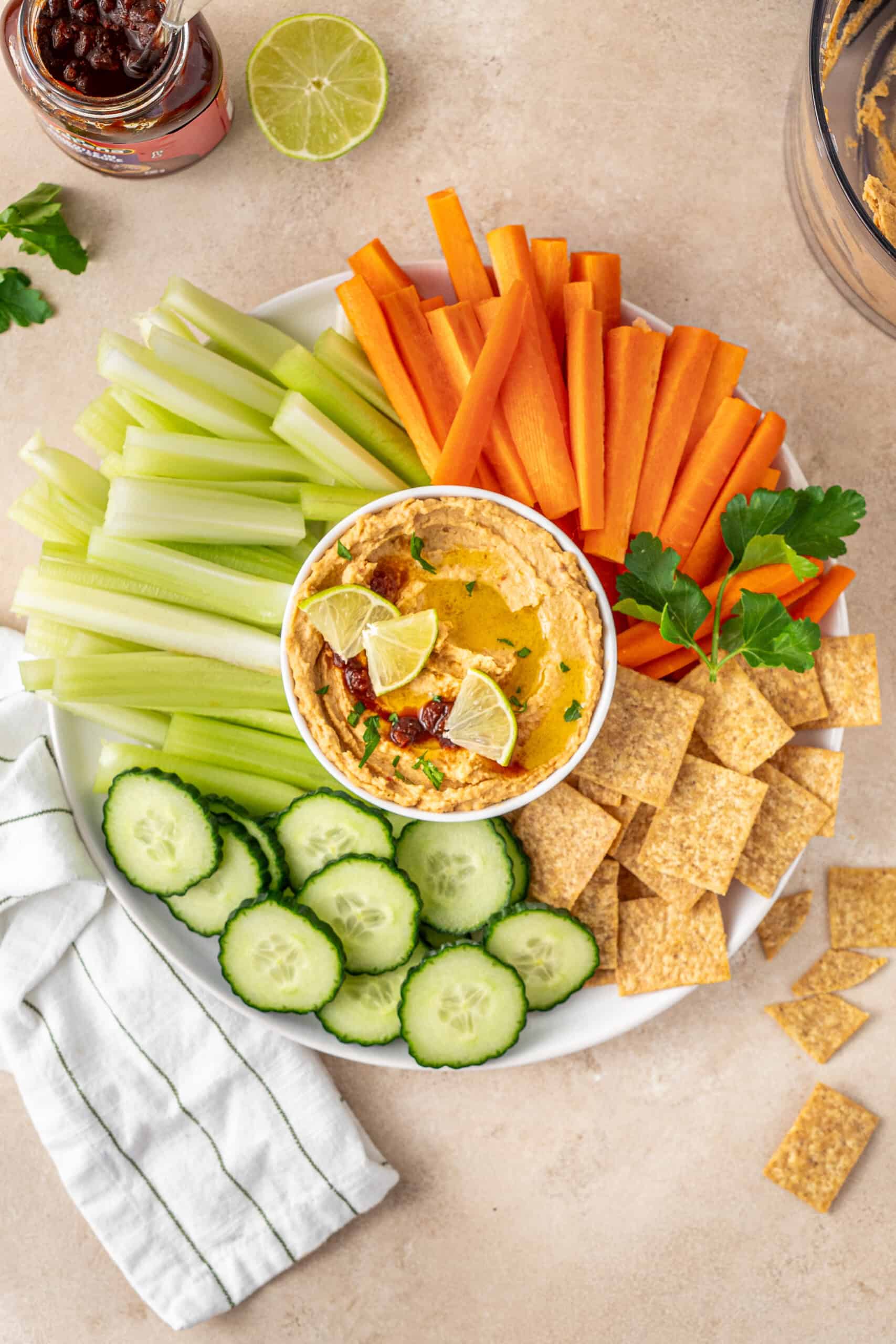 A plate with hummus, veggie sticks and crackers.