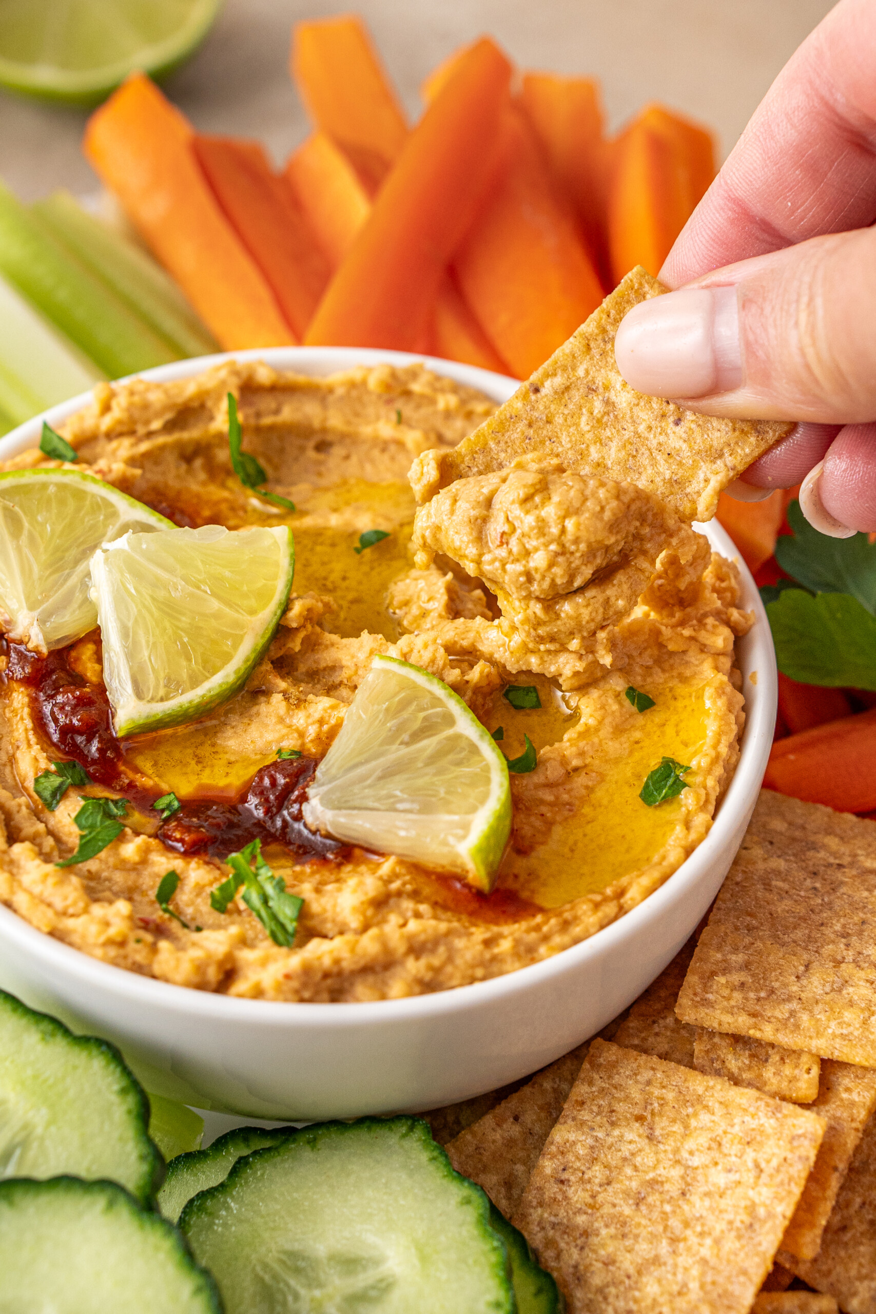 A hand dipping a cracker into a bowl of spicy chipotle hummus.