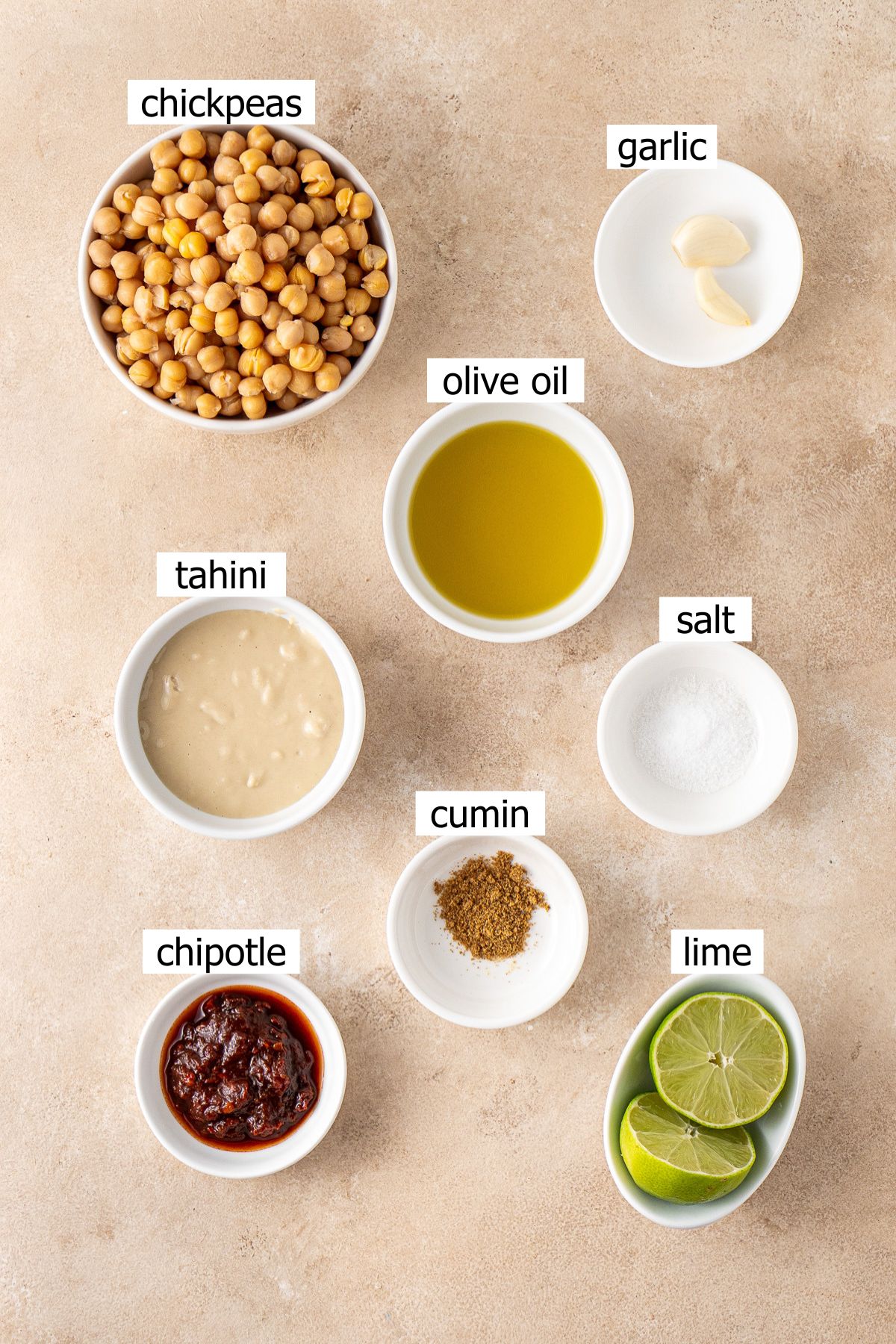 All ingredients needed to make homemade chipotle hummus laid out in small bowls.
