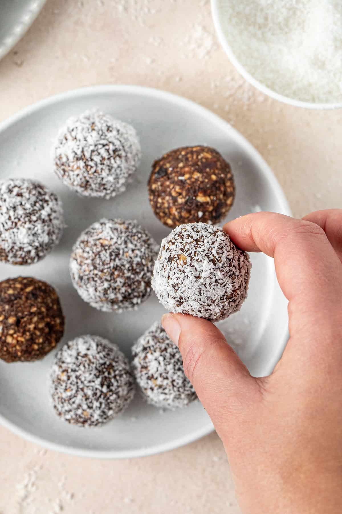 A hand picking up a cherry ripe bliss ball from a plate. 