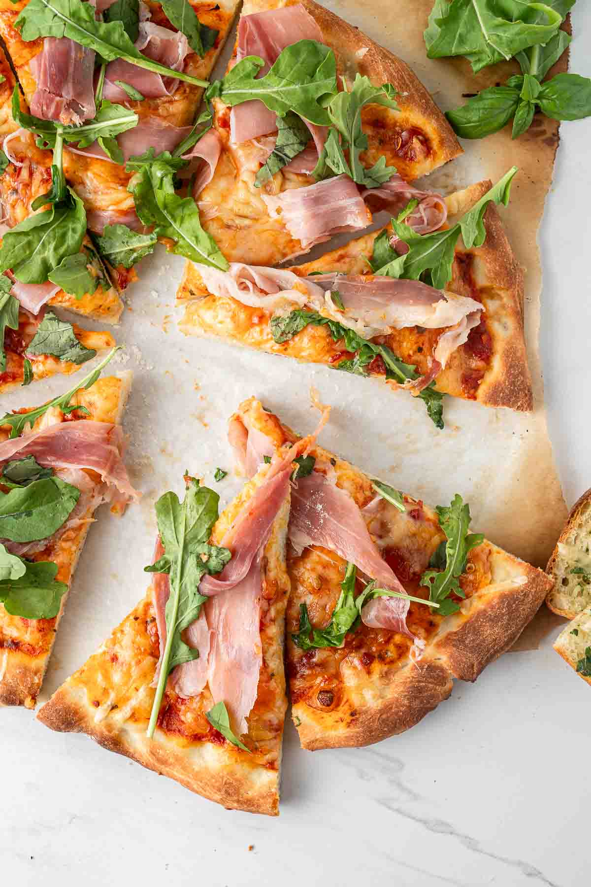 Prosciutto pizza with rocket and basil cut into slices.