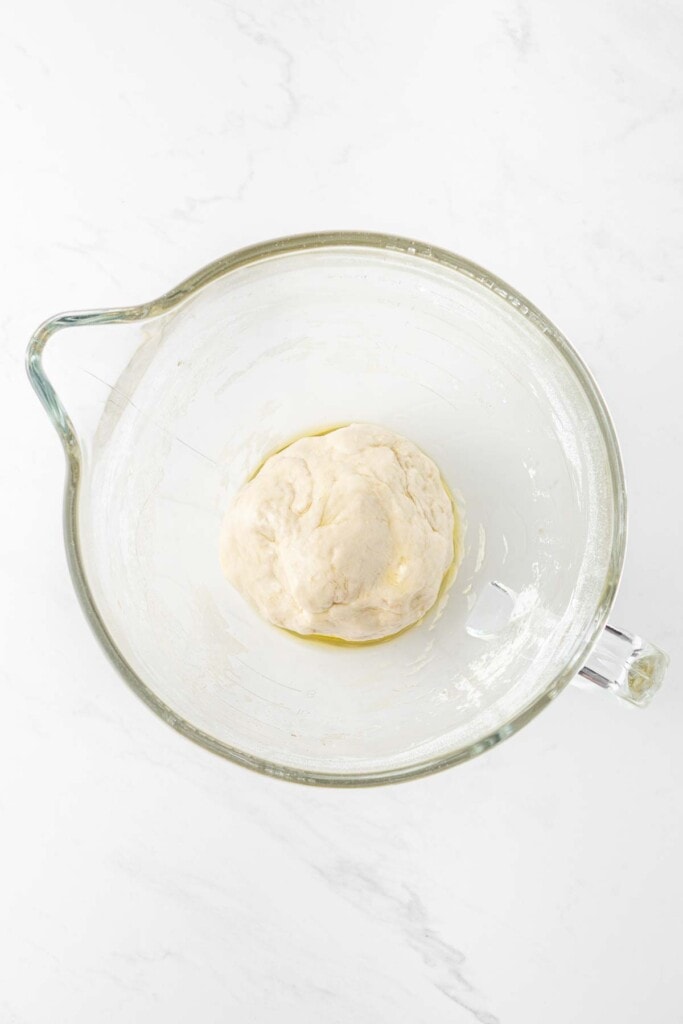 Pizza dough in a large glass mixing bowl.