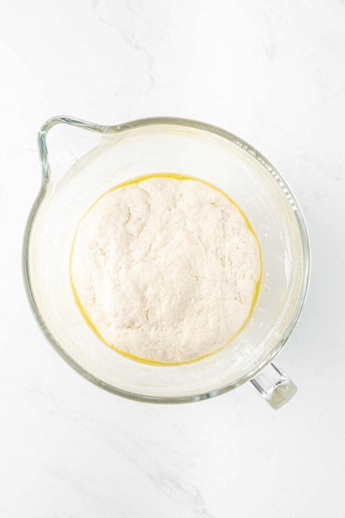 Pizza dough doubled in size in a large glass mixing bowl.