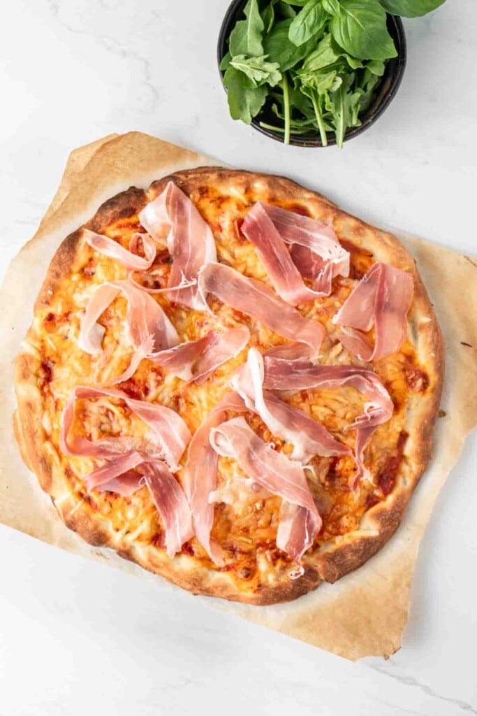Cooked pizza with pieces of prosciutto on top.