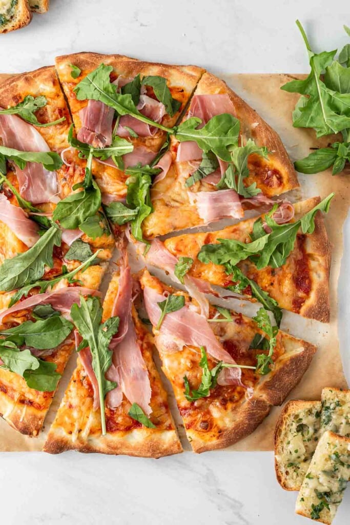 A prosciutto pizza cut into slices with rocket.