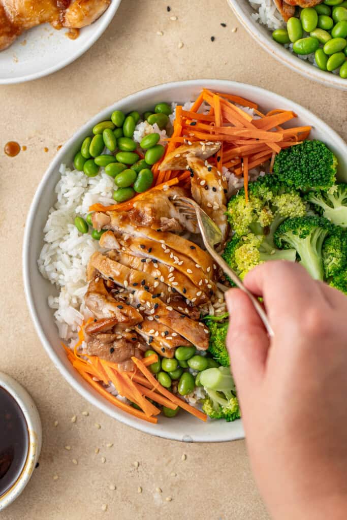A hand with a fork taking a bite of chicken teriyaki rice bowls.