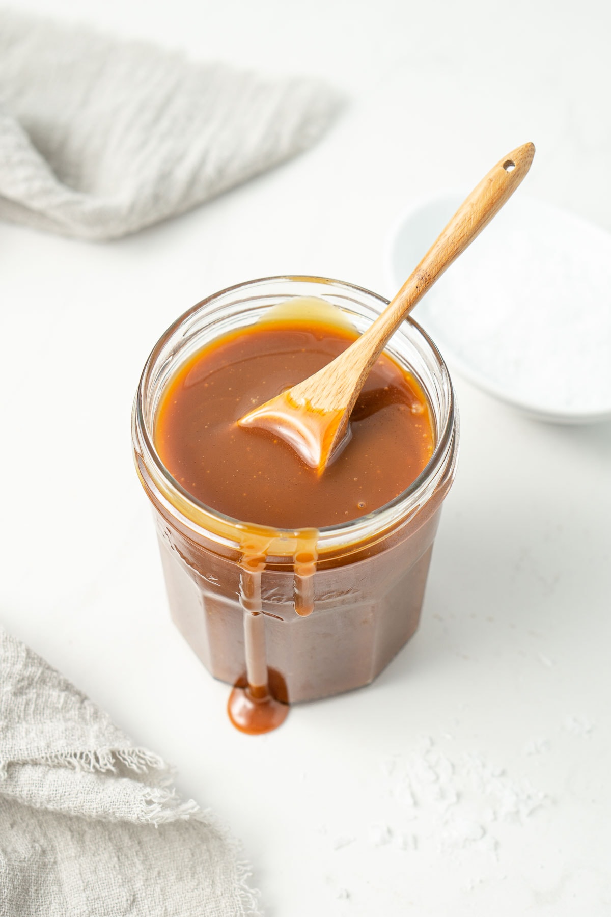 Vegan salted caramel sauce in a glass jar with a wooden spoon.