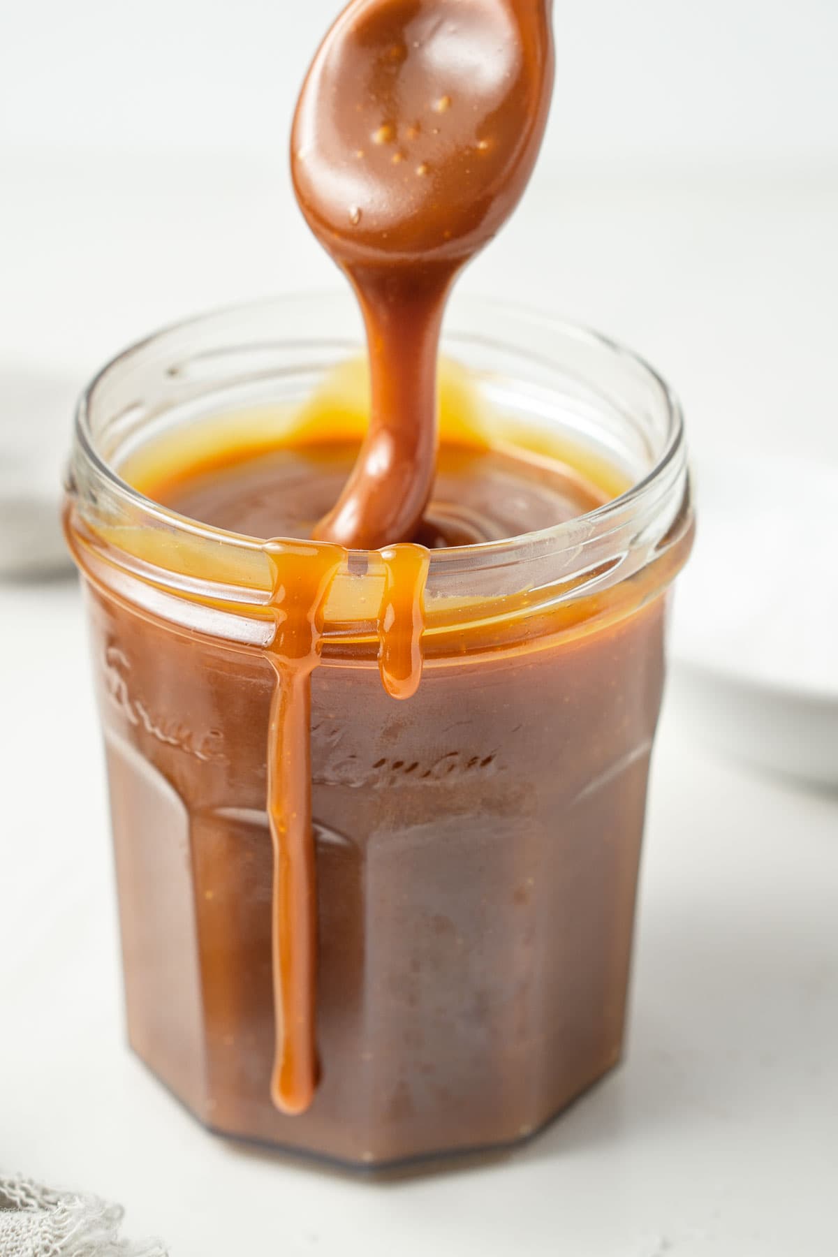 Close up of a thick drizzle of salted caramel in a glass jar.