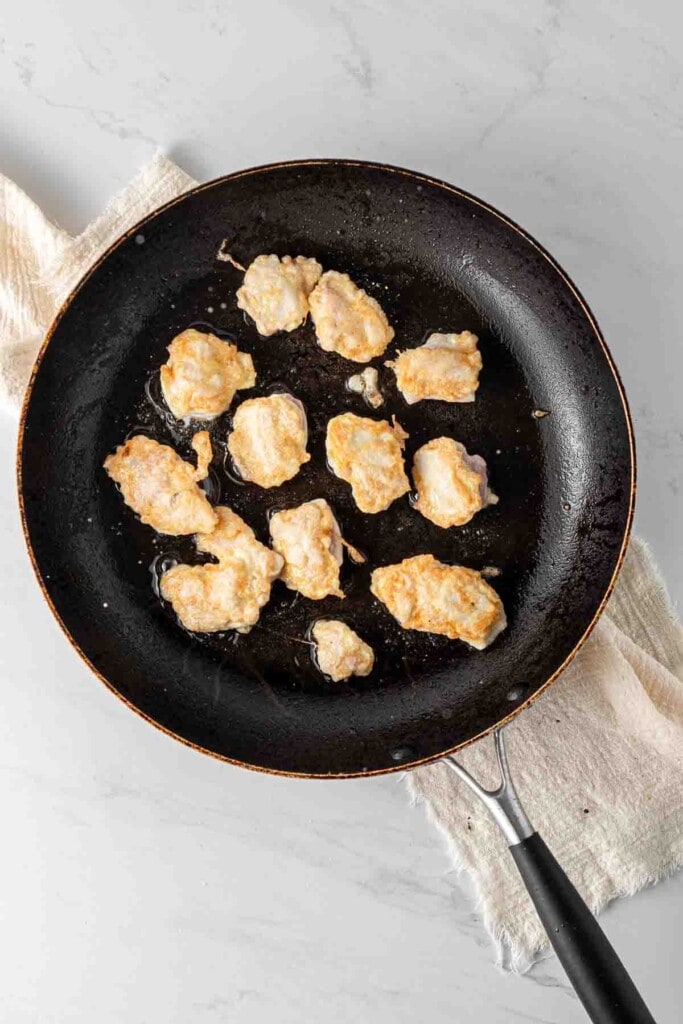 Cooking chicken pieces in a frying pan.