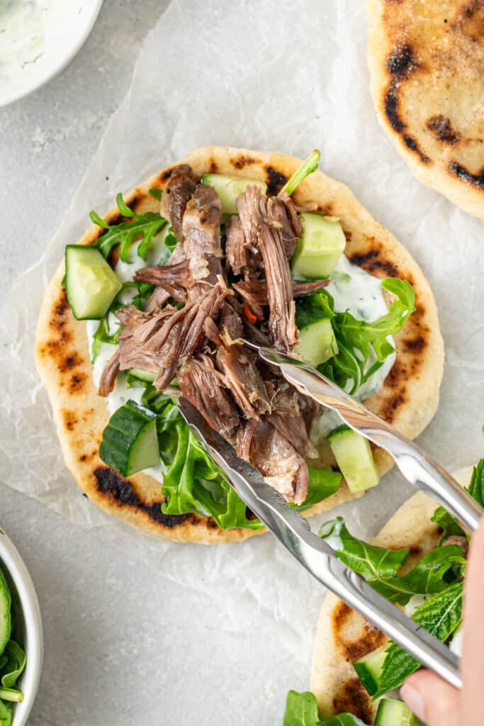 Adding the shredded lamb to the pitas.