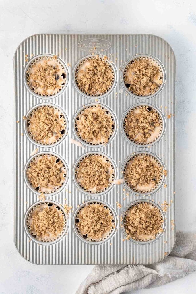 Muffin batter with a crumble topping in a muffin pan.