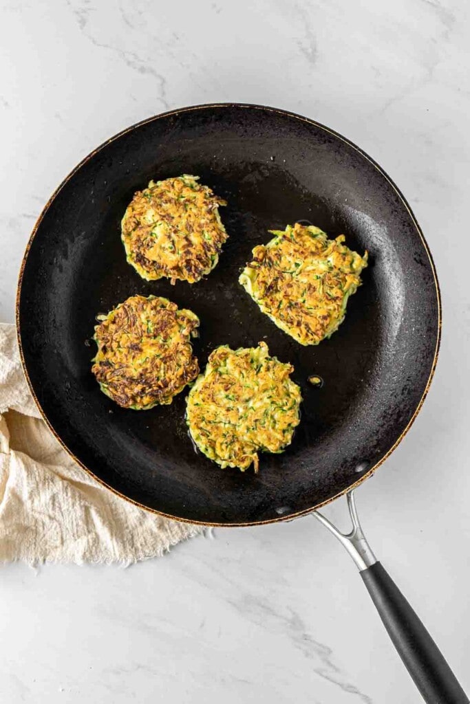 Fritters flipped over in a pan cooking looking crispy and golden.