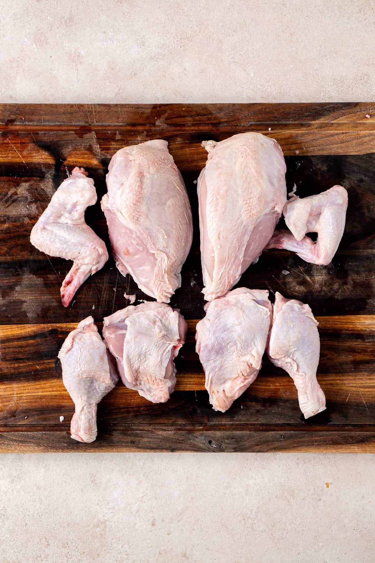 A whole chicken cut down into 8 pieces on a timber board.