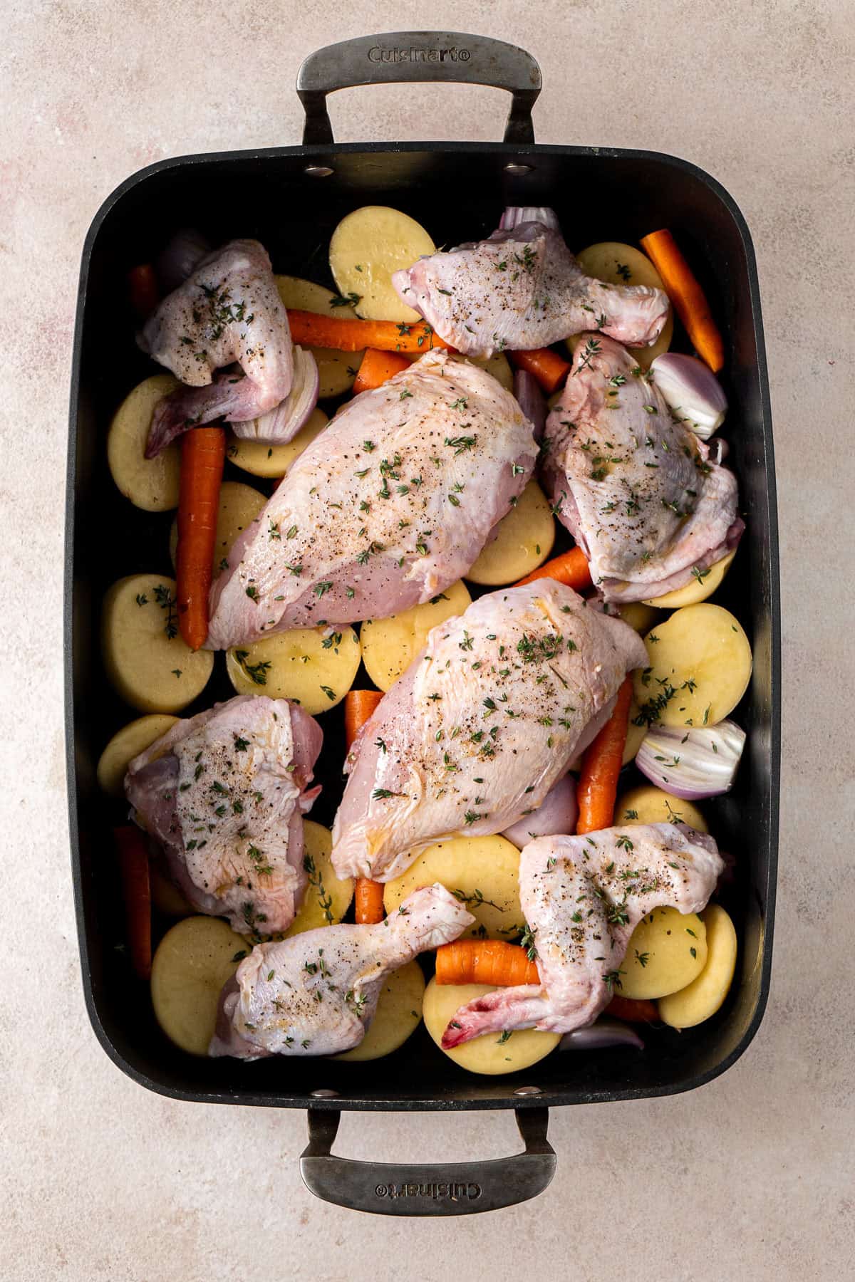 The chicken laid over the vegetables in a roasting pan.