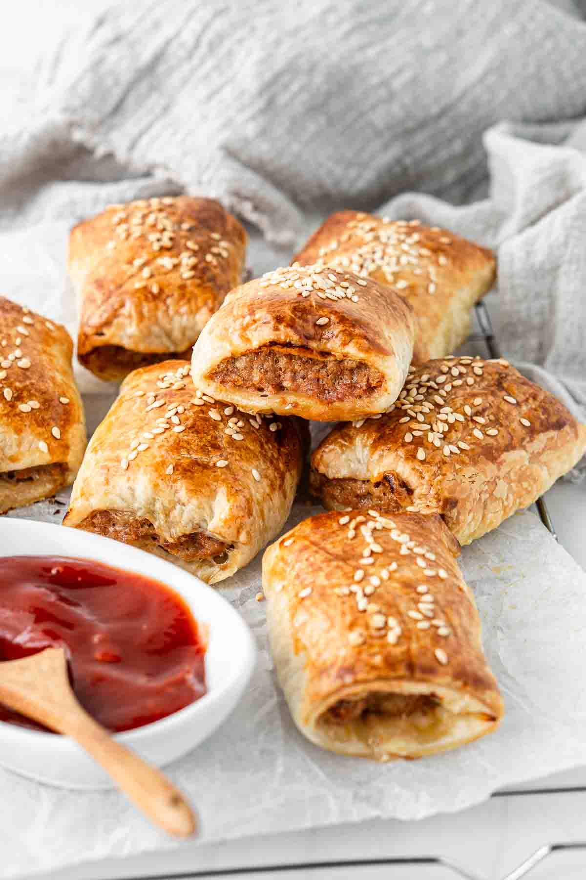 Sausage rolls stacked on a wire rack with tomato sauce. 