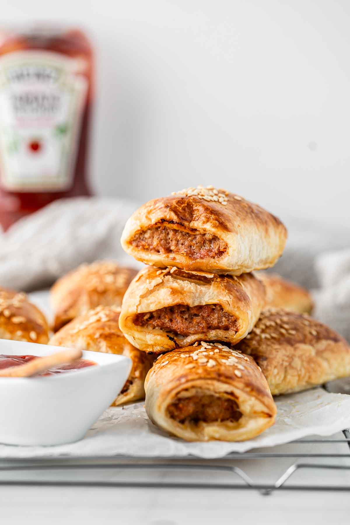 Sausage rolls stacked on top of each other with tomato ketchup. 