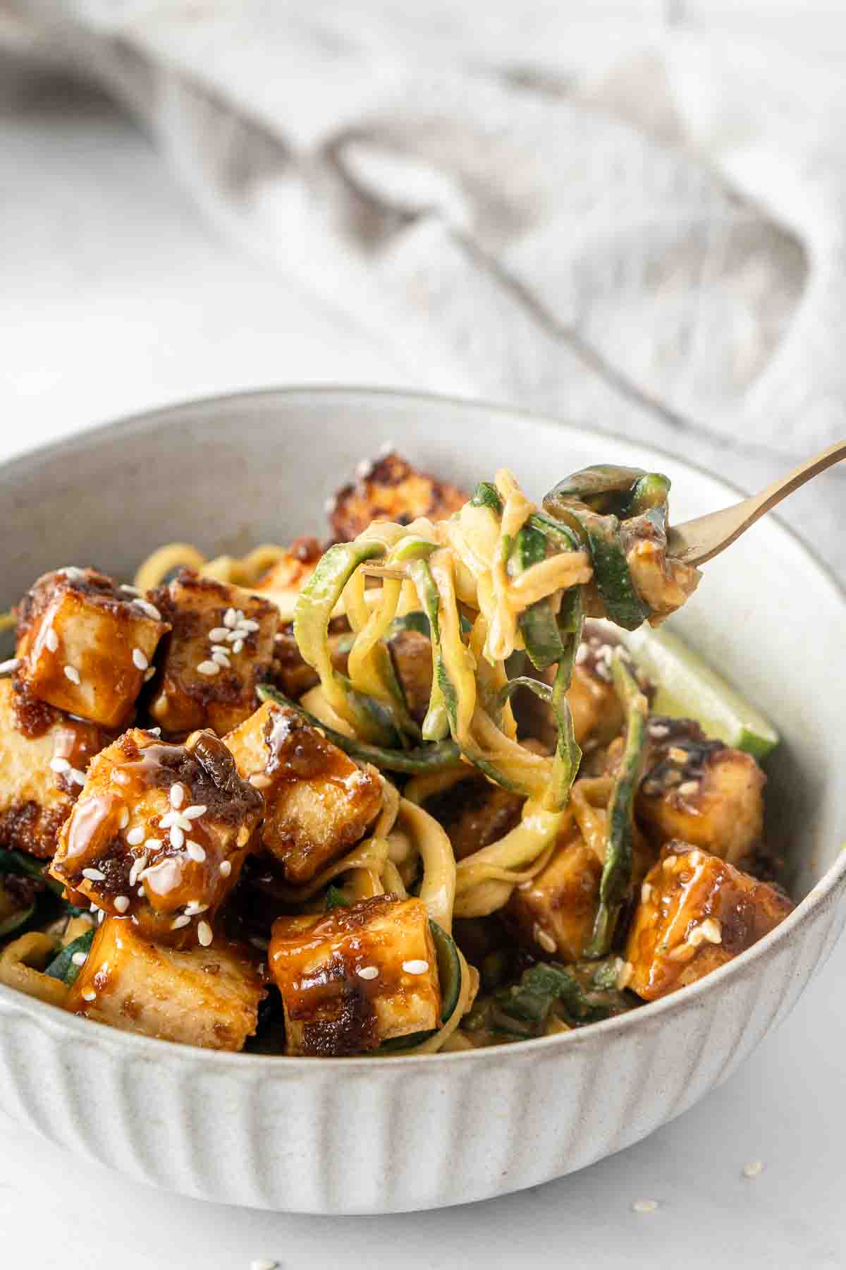 Close up of a fork full of creamy peanut zoodles with crispy tofu.