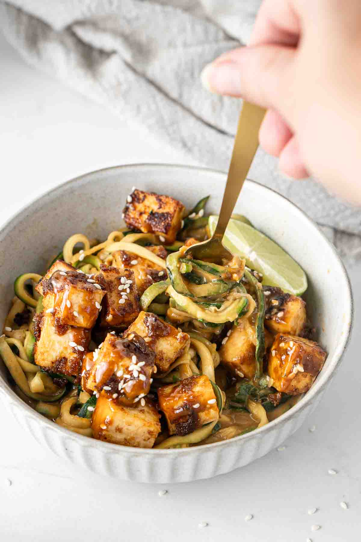 Bowl of crispy tofu with a fork getting a bite of saucy peanut zoodles.