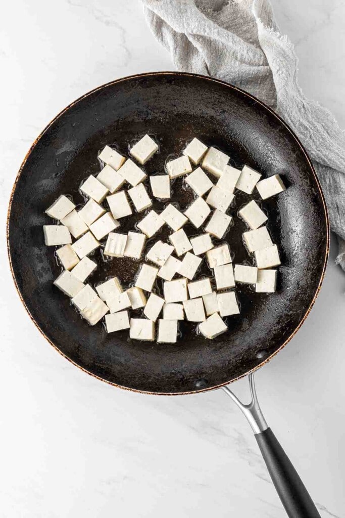 Cubed firm tofu in a frying pan.