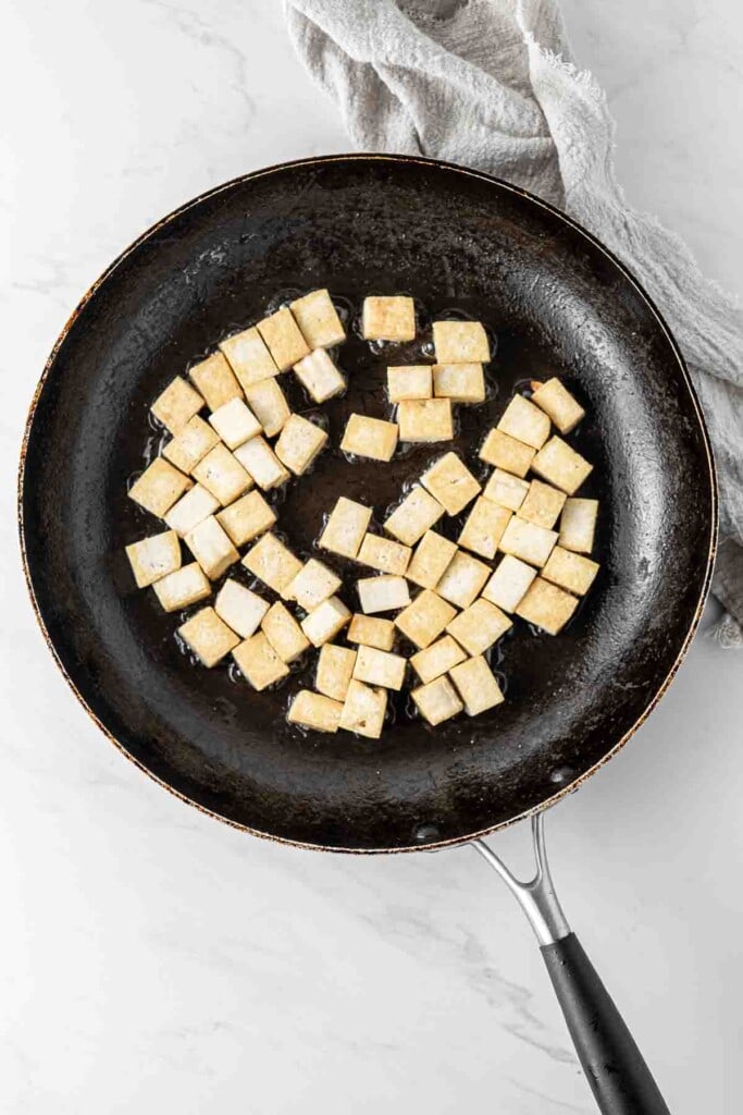 Browning cubed tofu in a frying pan.