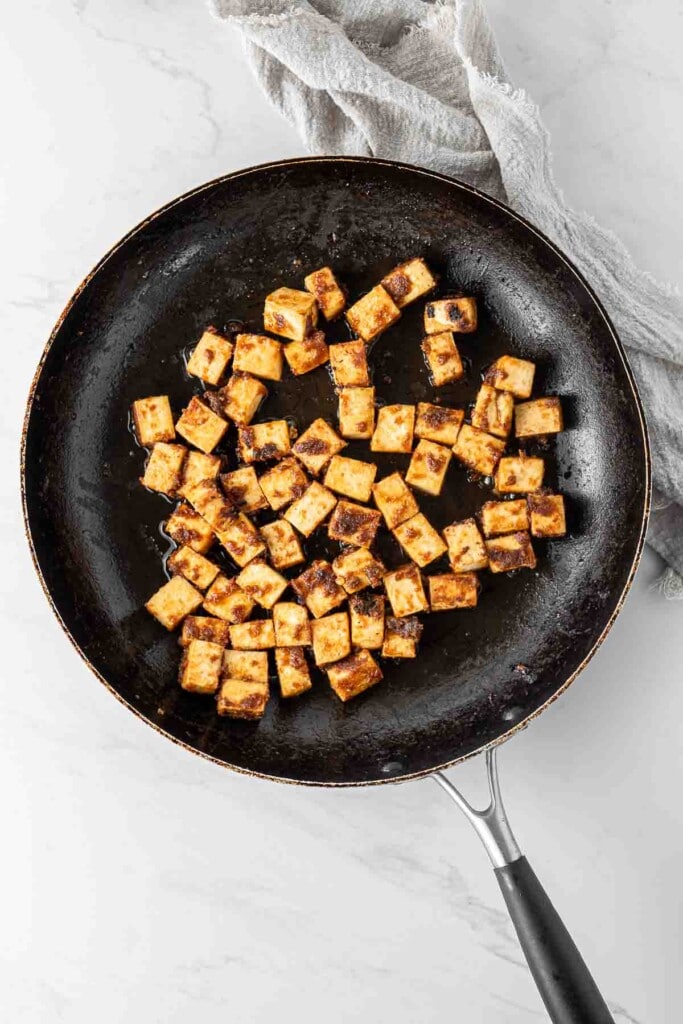 Crispy tofu cooking in the sauce in a frying pan.