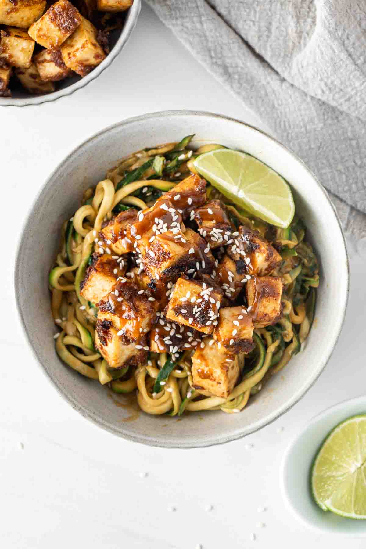 Crispy tofu and zoodles in a peanut sauce in a bowl with a wedge of lime.