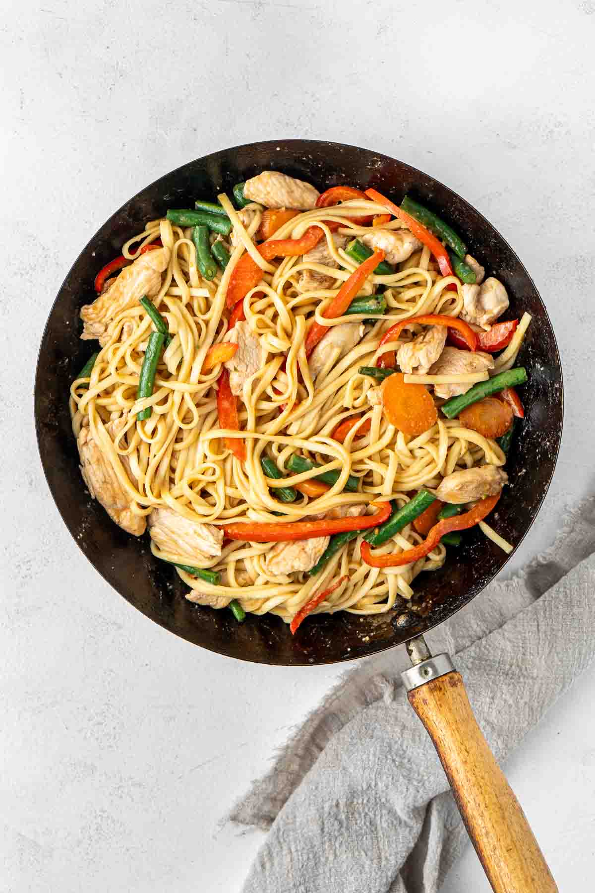 Chicken satay noodles with vegetables in a wok.