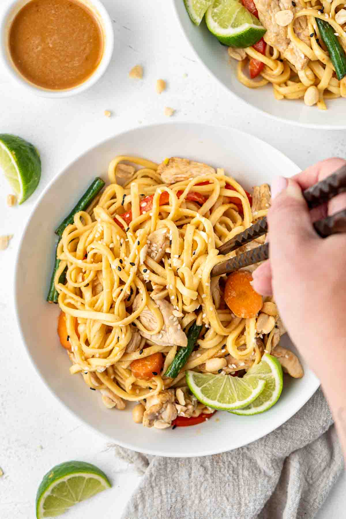 A hand taking a bite of chicken satay noodles with chopsticks.