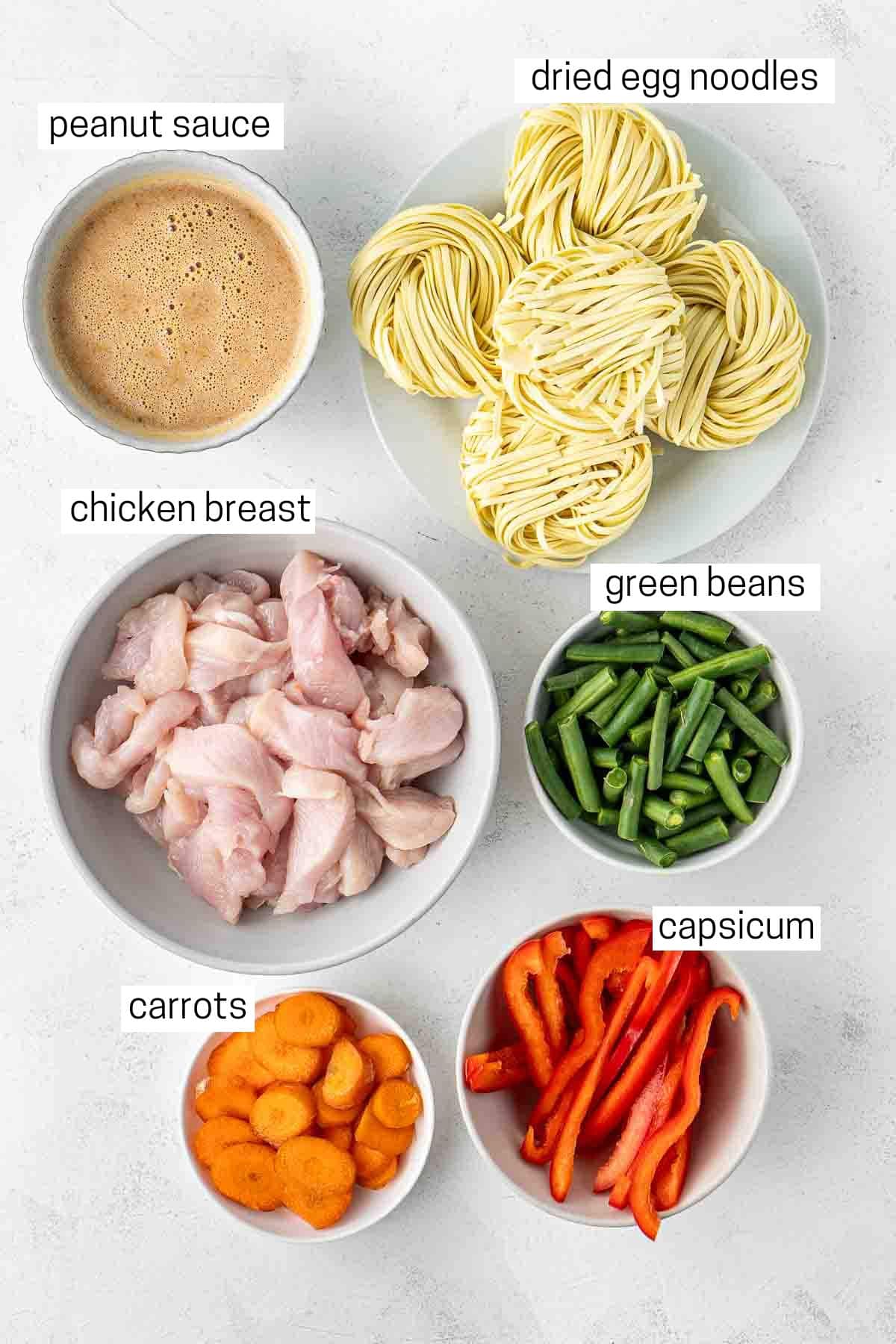 All ingredients needed to make chicken satay noodles laid out in bowls.