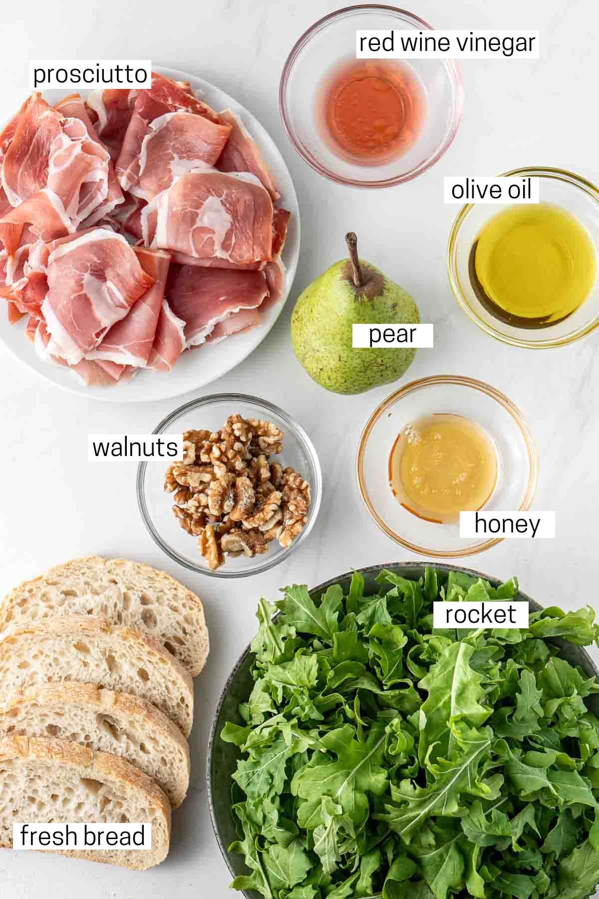 All ingredients needed for pear and prosciutto salad laid out in bowls.