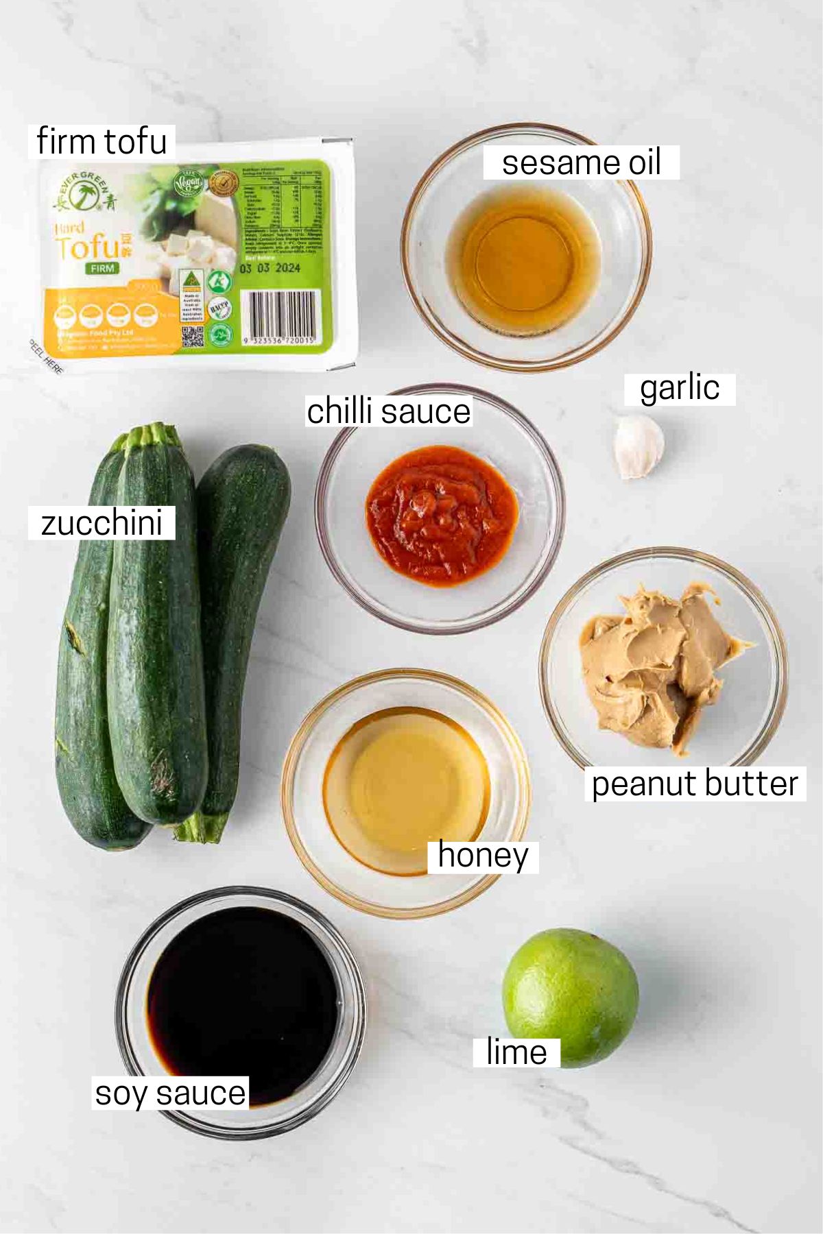 All ingredients needed to make crispy tofu and zoodles with peanut sauce laid out in small bowls.