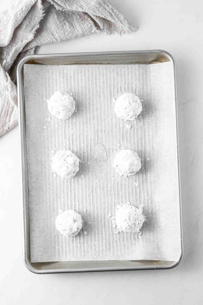 Balls of cookie dough coated in powdered sugar ready to bake on a tray.