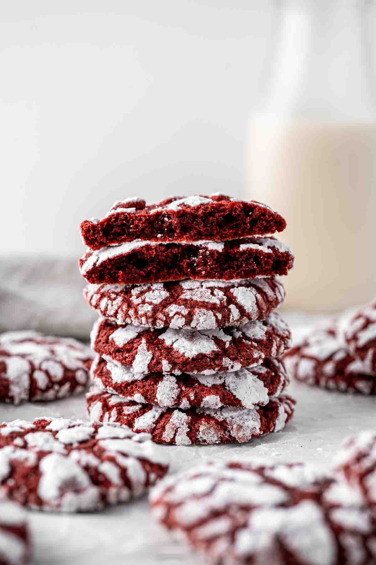 Stack of red velvet crinkle cookies with the top one broken in half revealing the fudgy vibrant centre. 