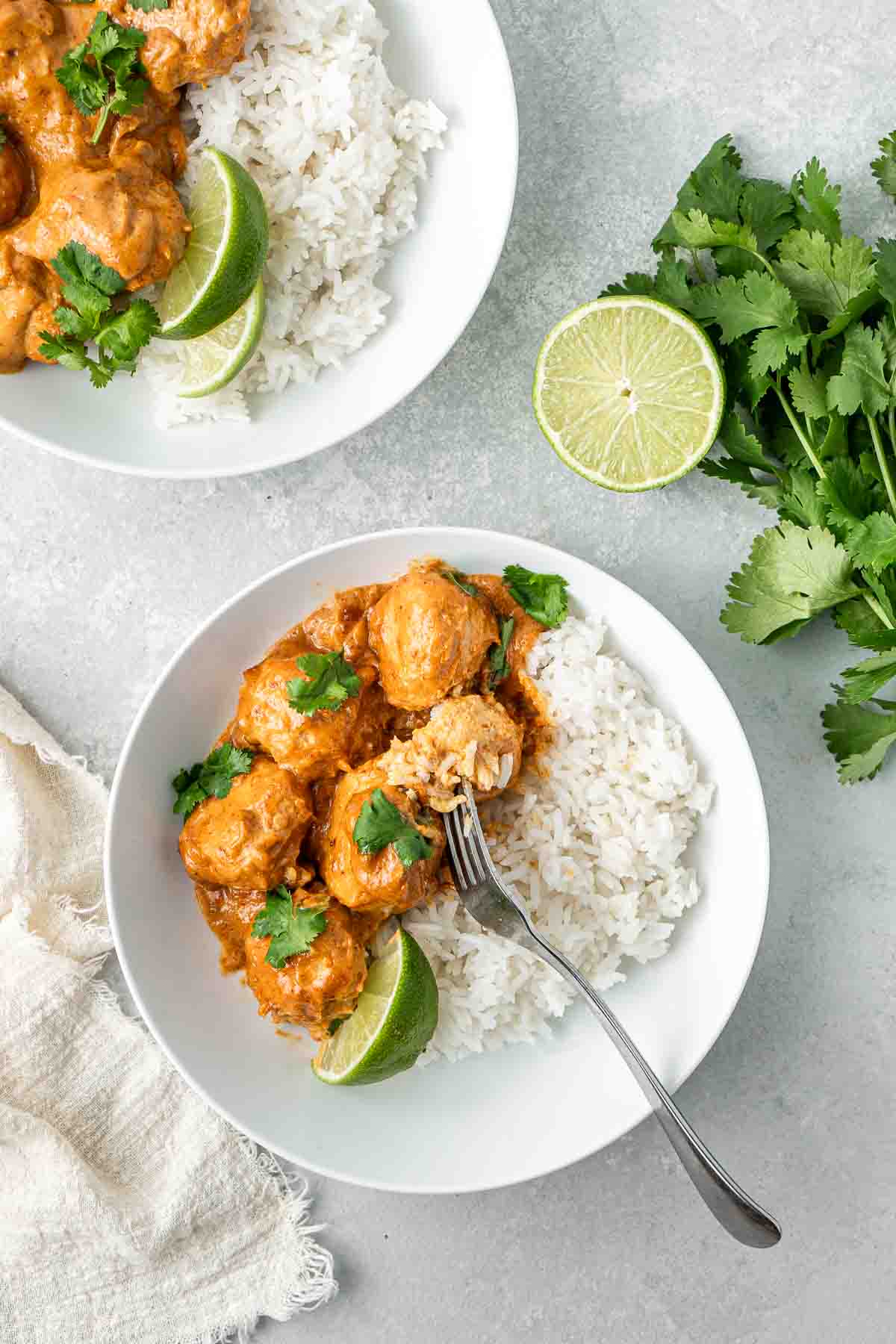 Thai red curry with baked chicken meatballs served on a white plate with rice and a fork taking a bite.