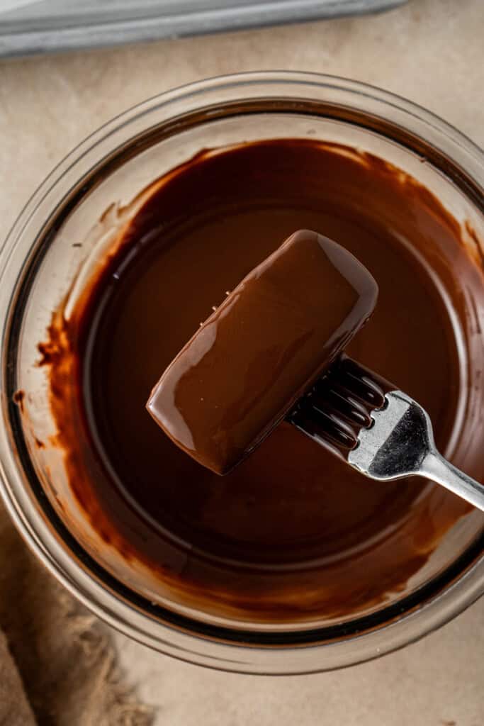 A fork dunking the biscuit into the chocolate to coat it.