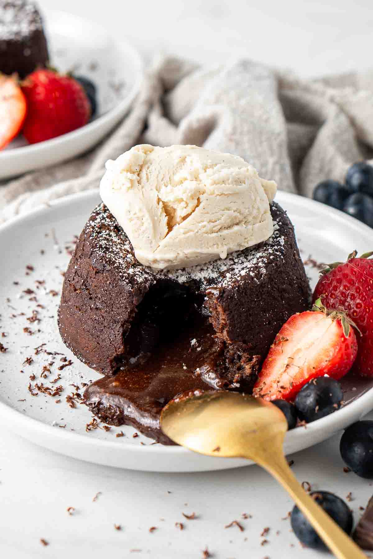 Dairy free lava cake cut open with a spoon served with berries and ice cream.