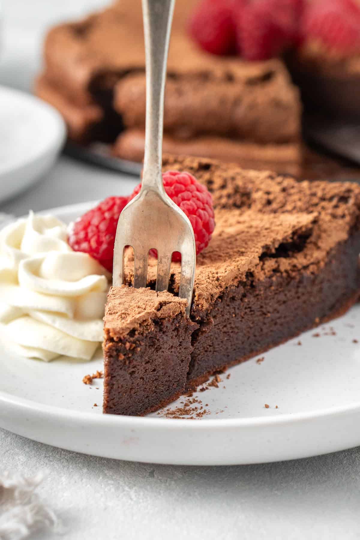 A fork taking a bite of flourless chocolate cake with raspberries.