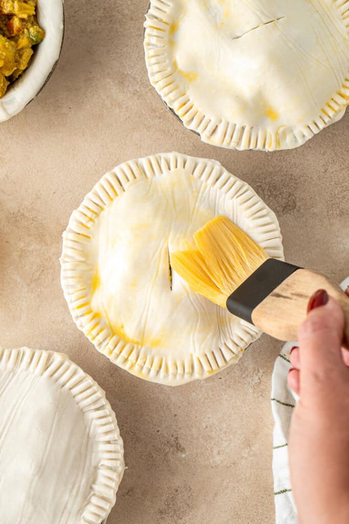 Brushing the tops of the pies with egg wash.