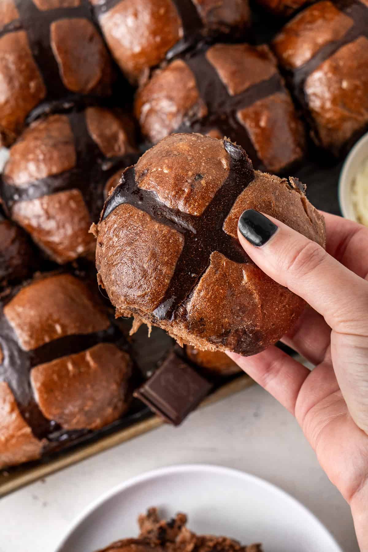 A hand picking up a chocolate hot cross bun.