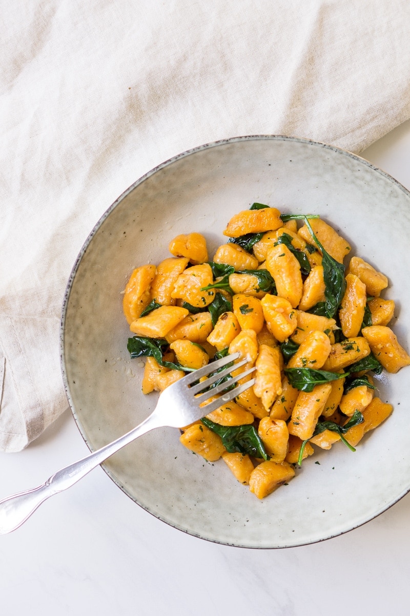 Sweet potato gnocchi with spinach and garlic in a bowl with a fork