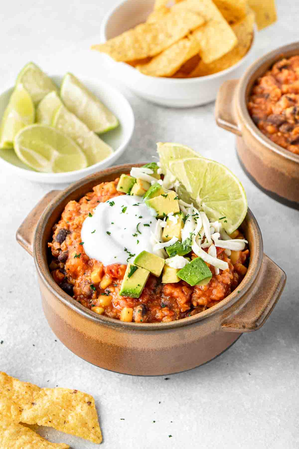Vegan chilli served in a bowl topped with vegan sour cream, avocado, cheese and lime.