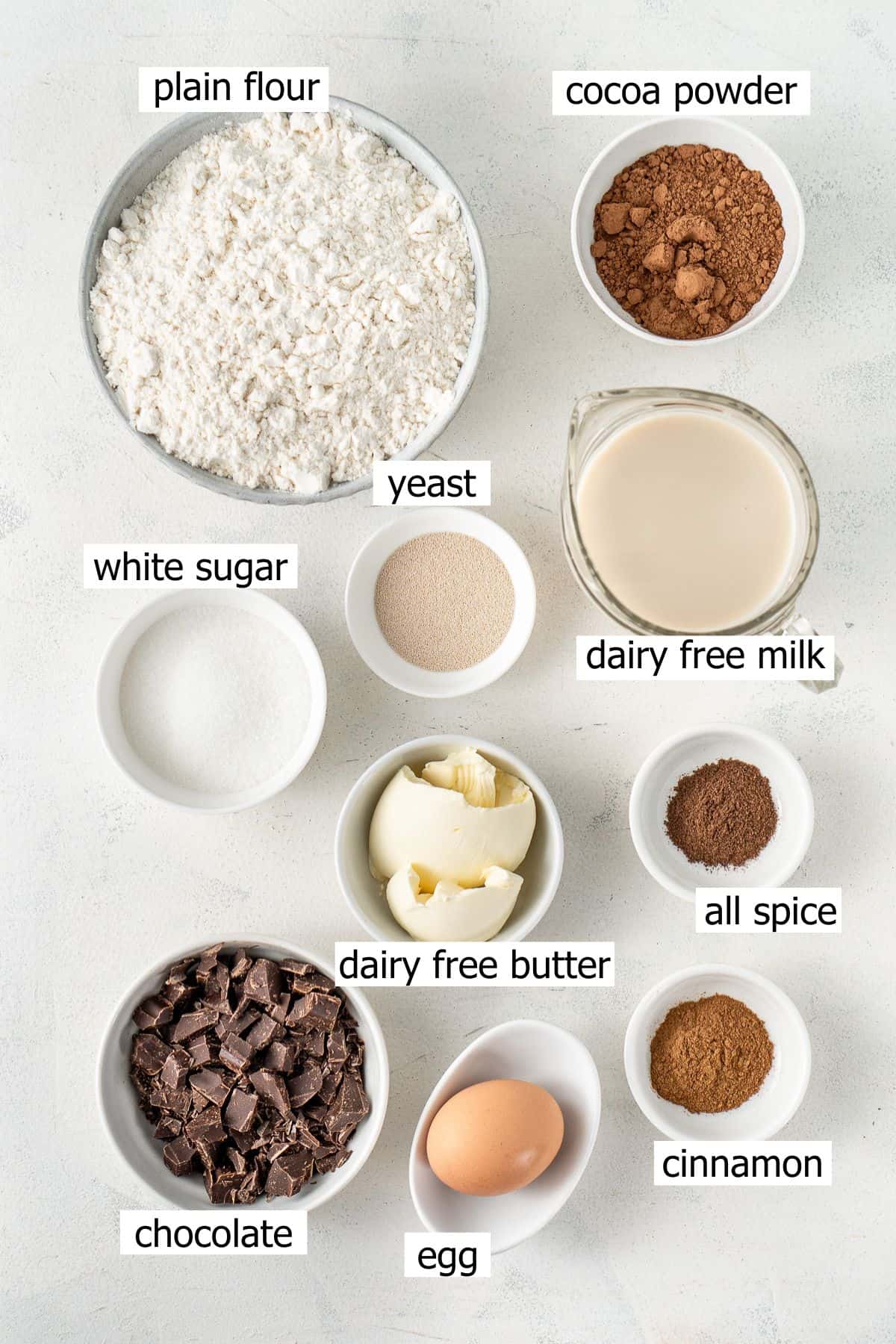 All ingredients needed to make chocolate hot cross buns laid out in small bowls.