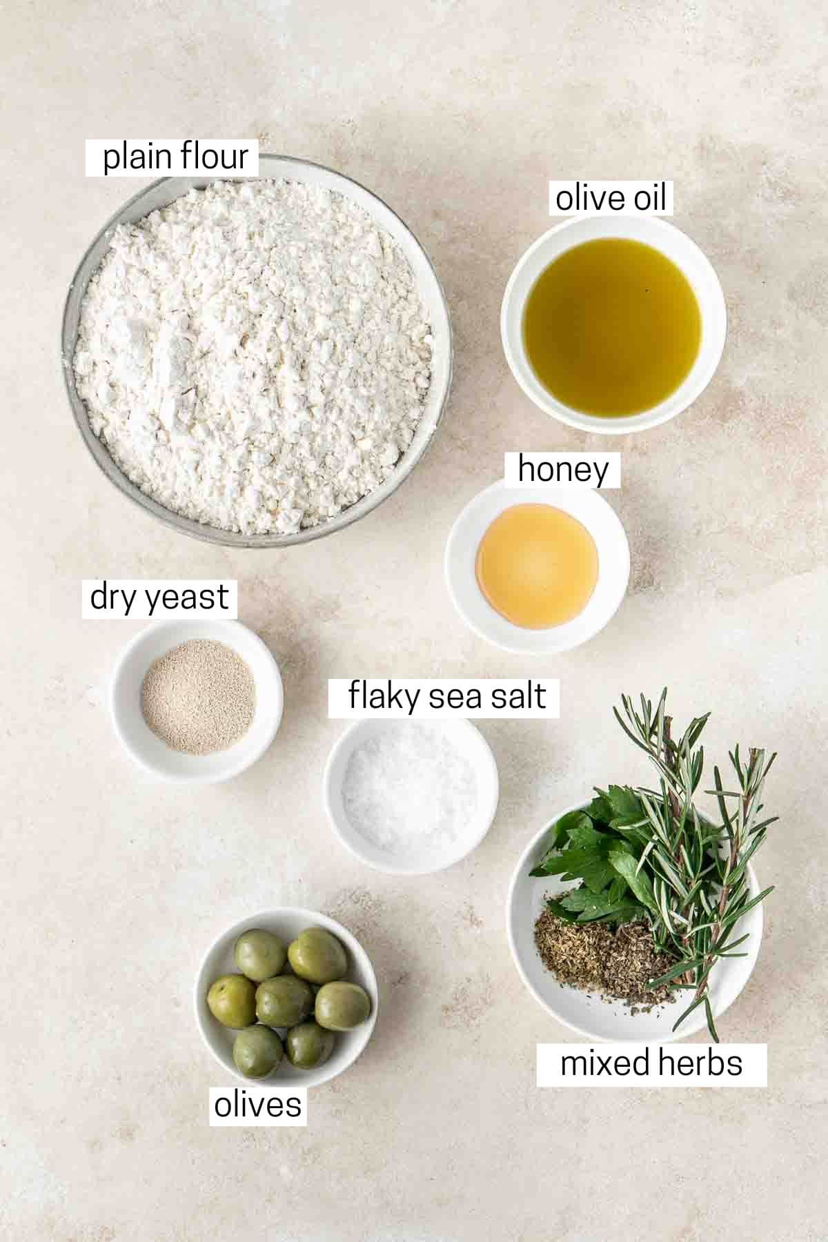 All ingredients needed to make olive and herb focaccia laid out in small bowls.