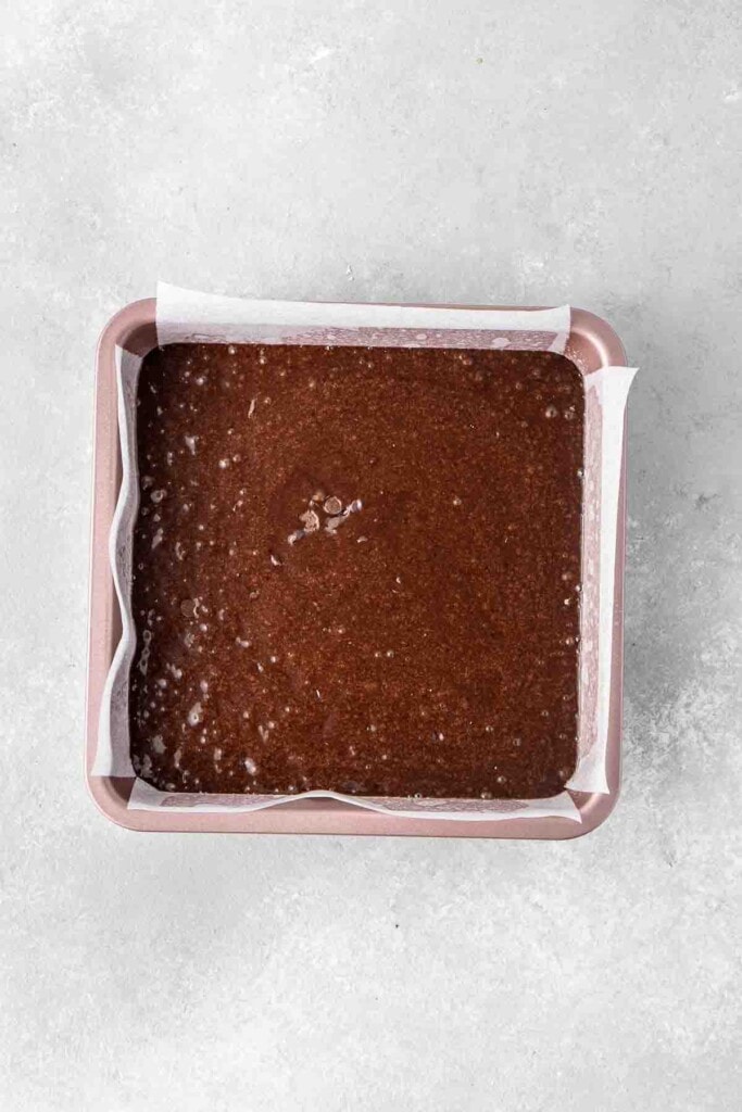 Brownie batter in a lined square baking tin.