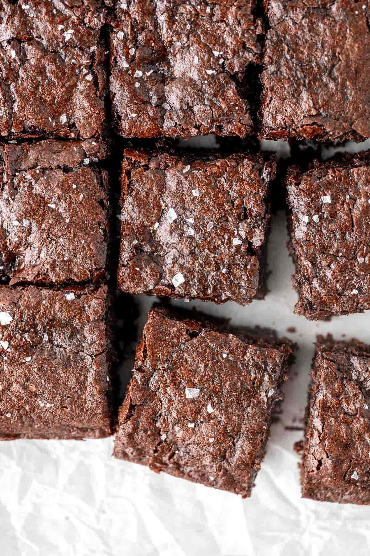 Vegan brownies cut into squares with shiny, crinkle tops and flaky sea salt. 