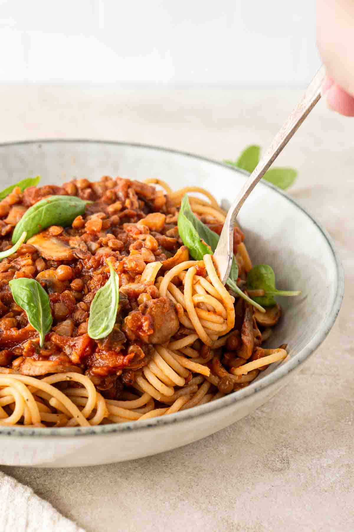 A fork twirling the spaghetti bolognese in a bowl with fresh basil.