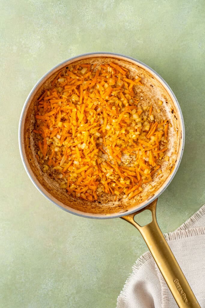 Sautéing the onions and carrots in a frying pan.