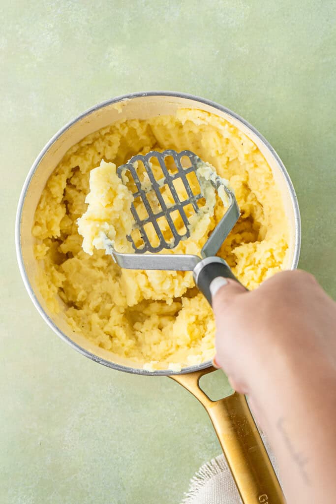 Mashing the potatoes in a pot.