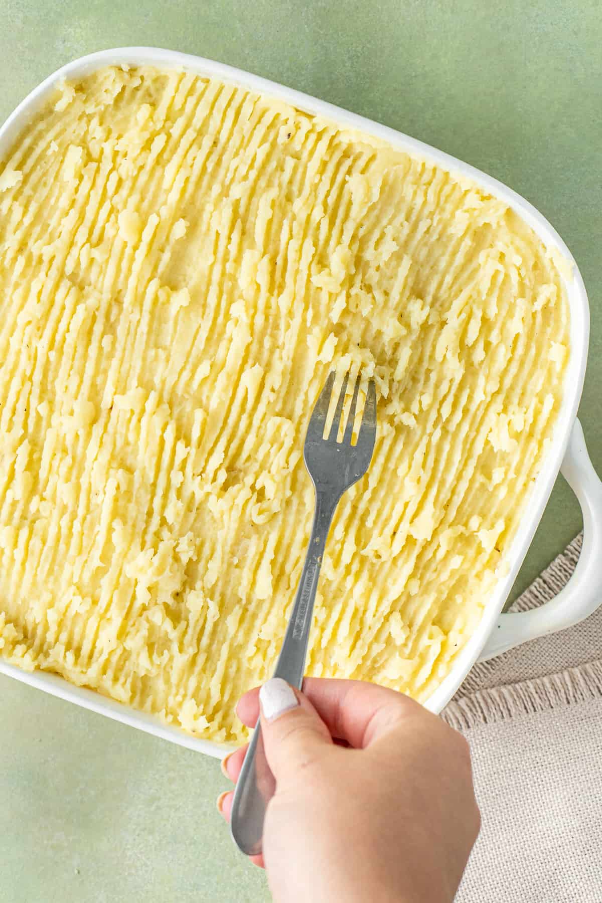 Using a fork to score the mashed potatoes on the pie.